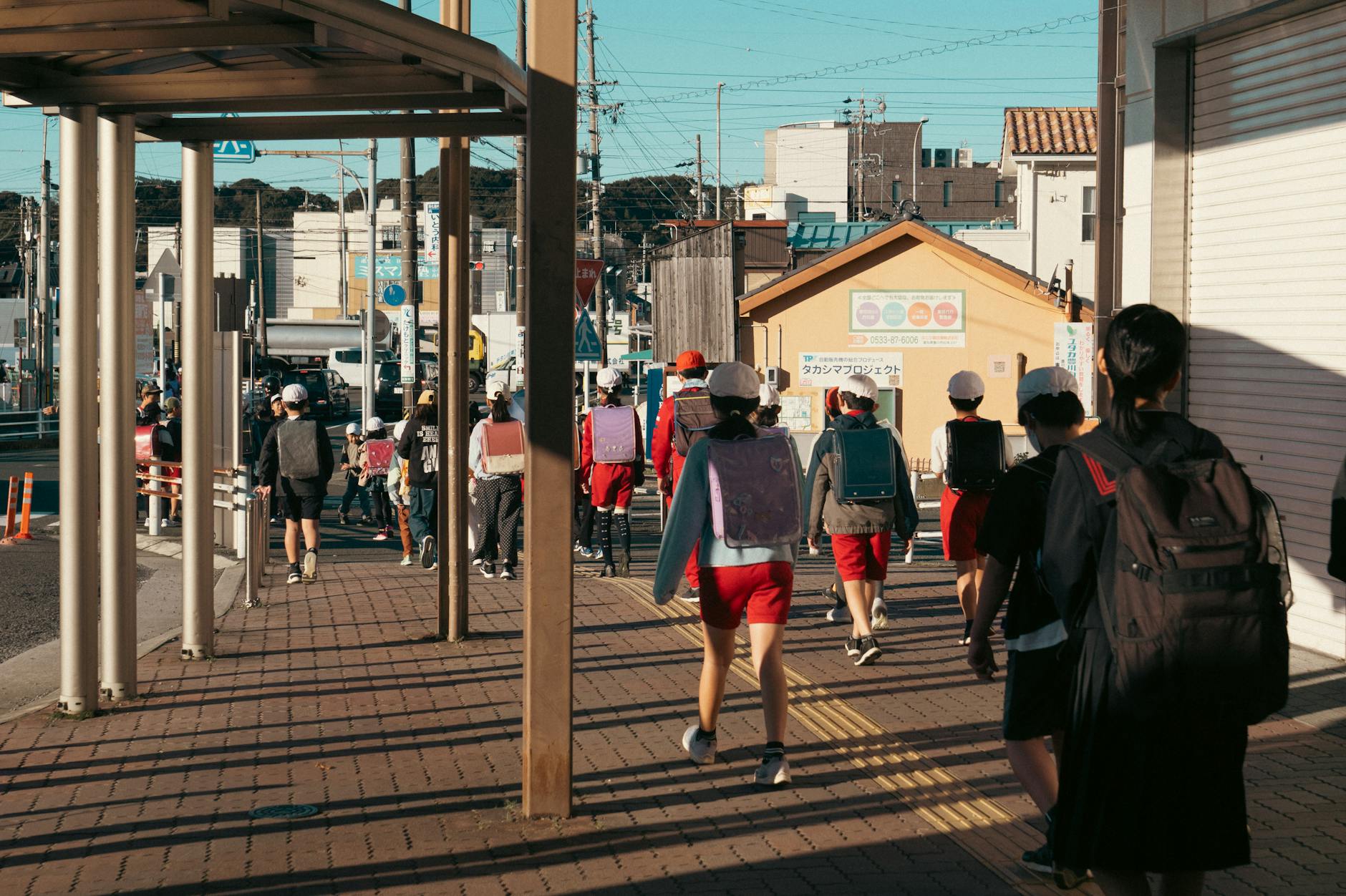 Uczniowie z plecakami idą chodnikiem w słoneczny dzień