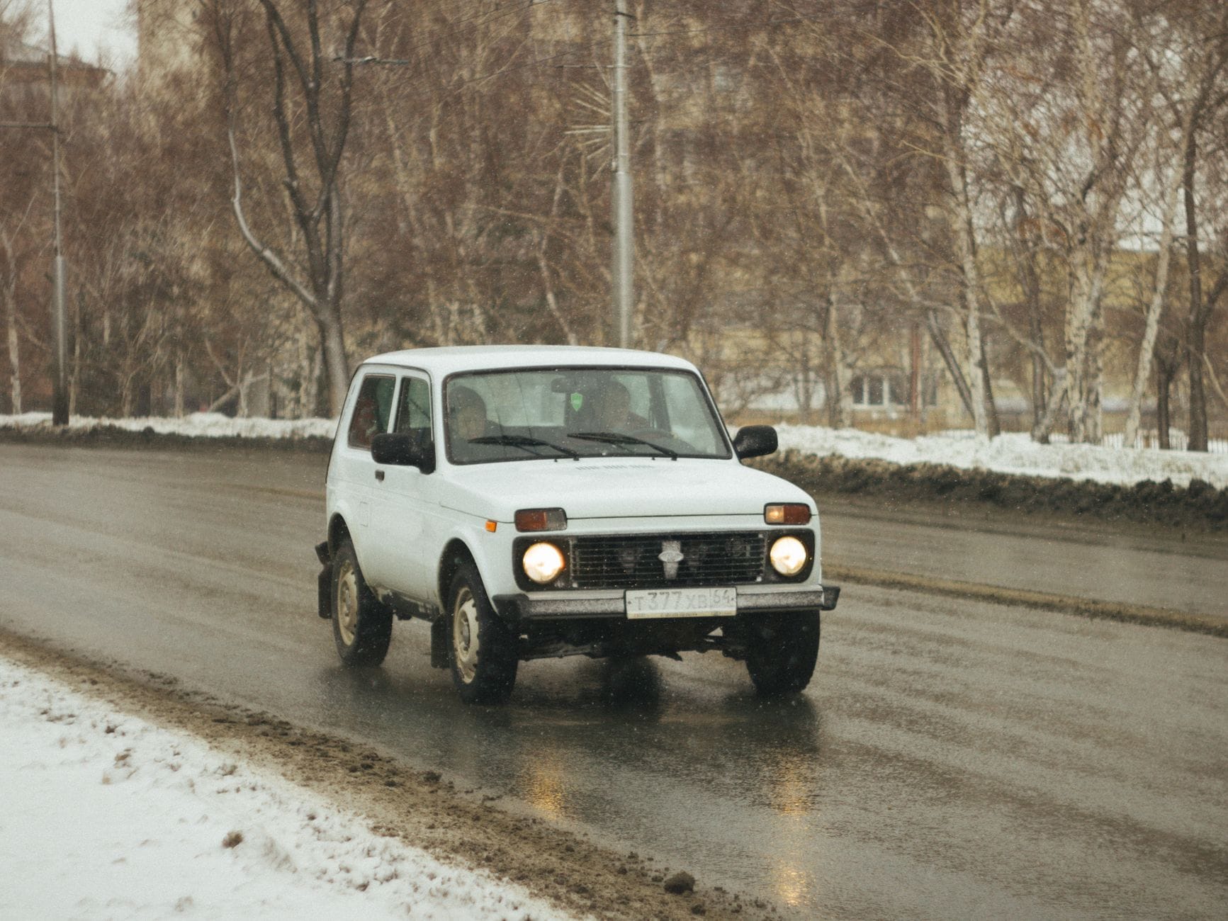 Białe terenowe auto jedzie po ośnieżonej, śliskiej ulicy w mieście