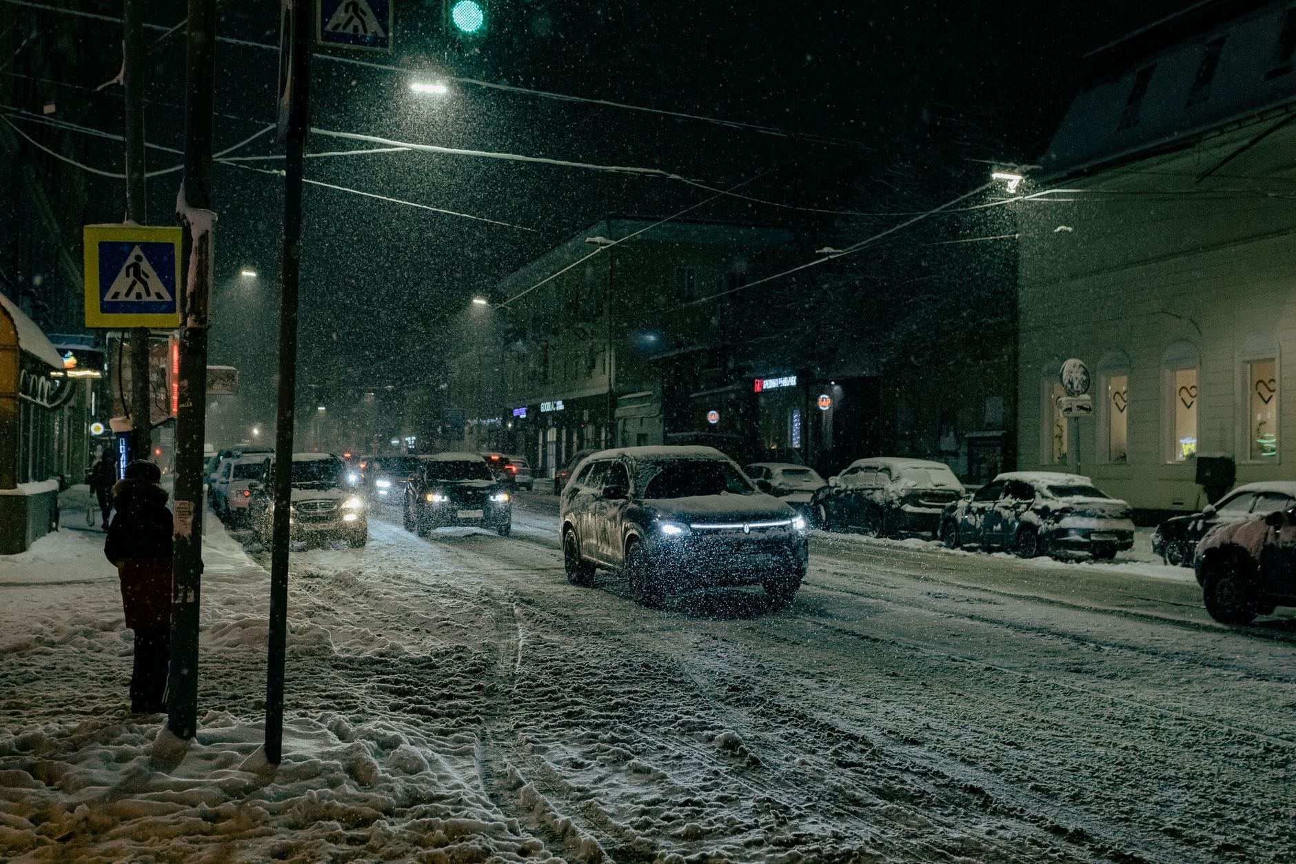 Nocna zaśnieżona ulica w mieście z jadącymi samochodami